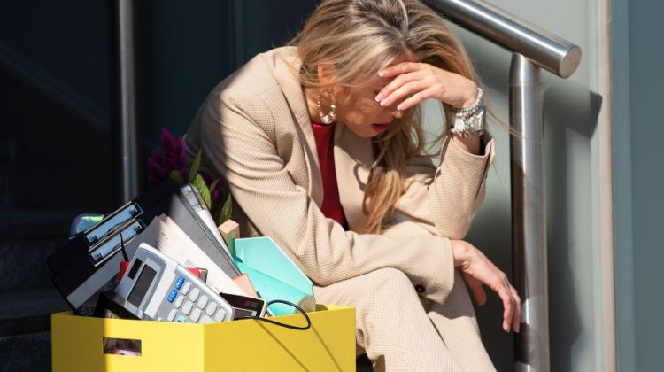 woman with box of belongings on steps after losing her job